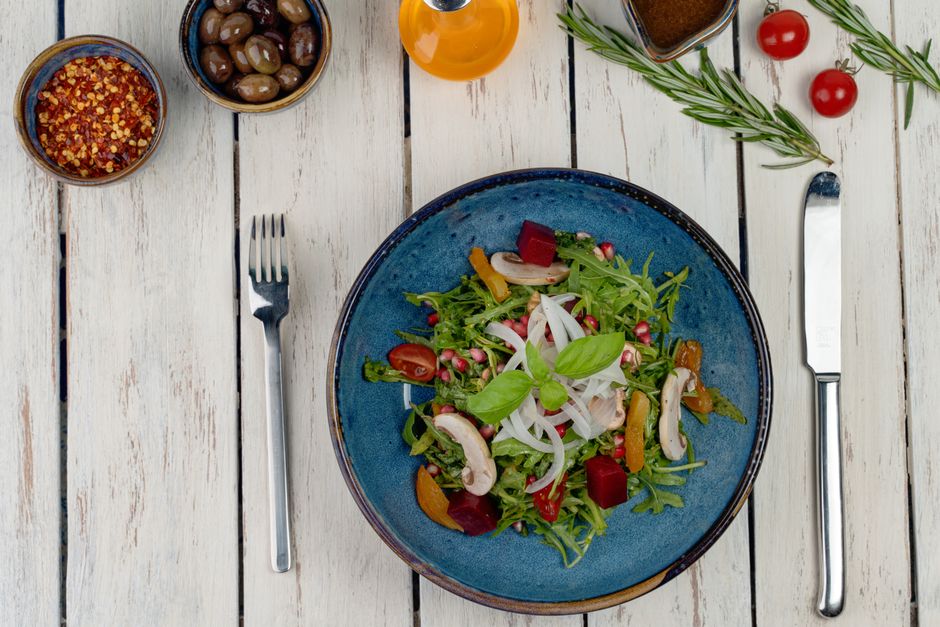 Fresh vegetable salad with mushrooms, olives, and pomegranate on a rustic table.
