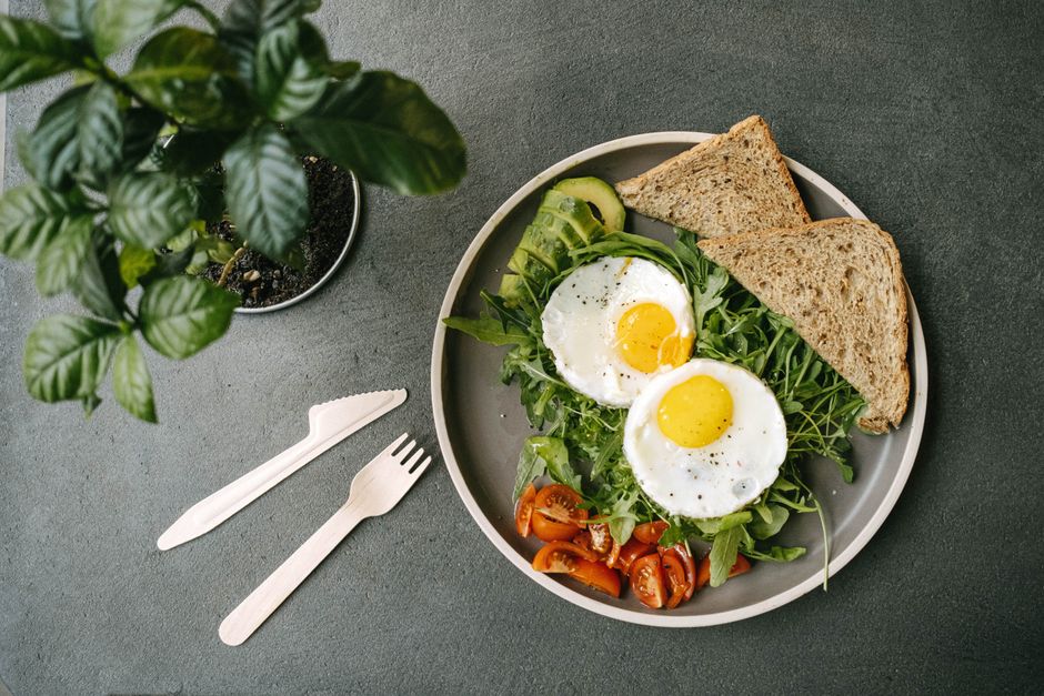 Top view of a fresh breakfast plate with eggs, toast, and salad on a gray surface.