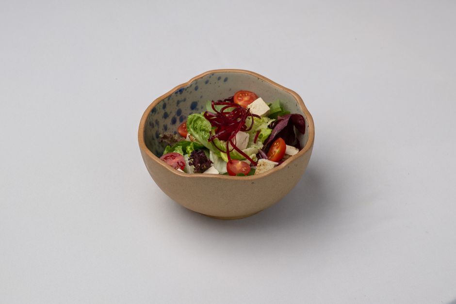 A vibrant mixed salad featuring tofu, cherry tomatoes, and greens in a ceramic bowl.