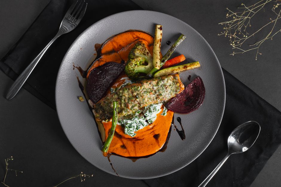Close-up of a gourmet vegetable dish with vibrant sauces on a dark plate viewed from above.