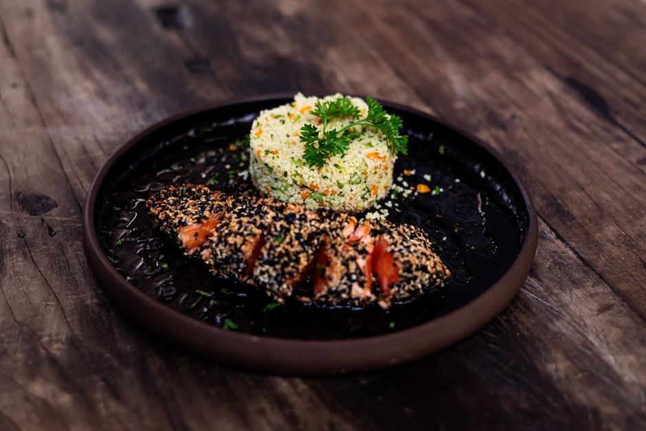 A delicious plate of seed-crusted fish paired with couscous garnished with herbs, served on a rustic wooden table.