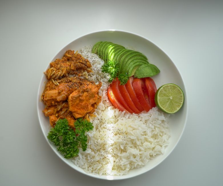 A colorful rice bowl with avocado, pork, tomato, and lime, perfect for a fresh meal.