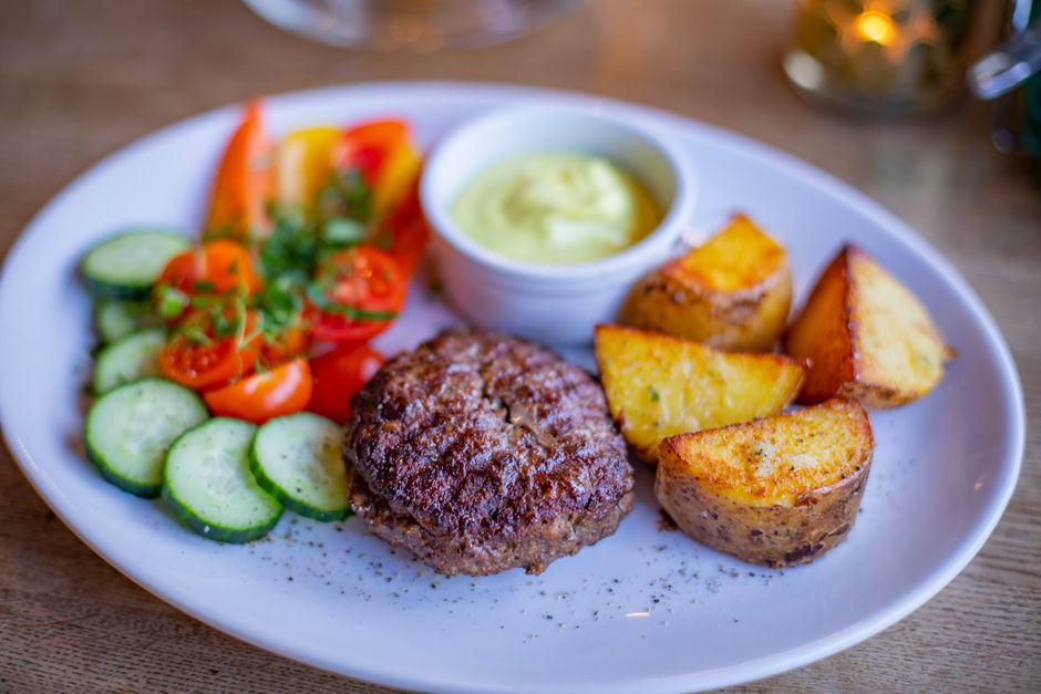 Close-up of a tasty grilled patty served with fresh vegetables, roasted potatoes, and sauce.