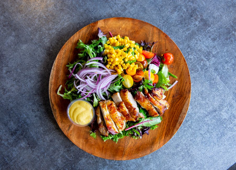 Delicious grilled chicken salad with veggies and dressing served on a wooden plate.