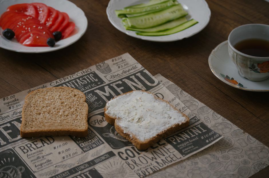 A rustic breakfast setup featuring bread, sliced cucumber, tomatoes, and tea on a wooden table.