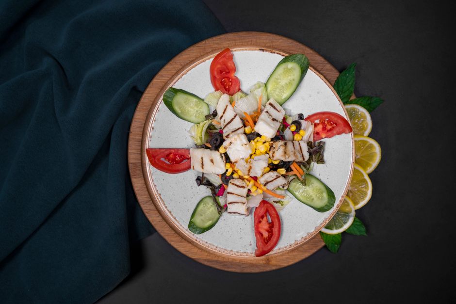 A vibrant grilled chicken salad featuring cucumbers, tomatoes, and corn beautifully arranged on a plate.