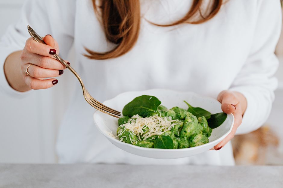 A delicious serving of spinach gnocchi with grated parmesan held by a woman.