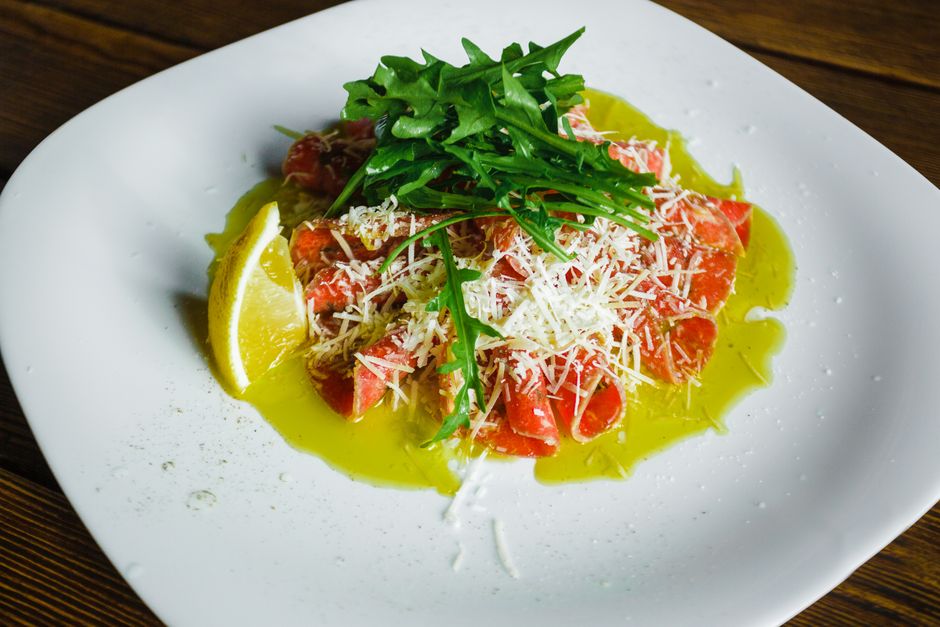 Salmon carpaccio garnished with arugula, cheese, lemon, and olive oil.