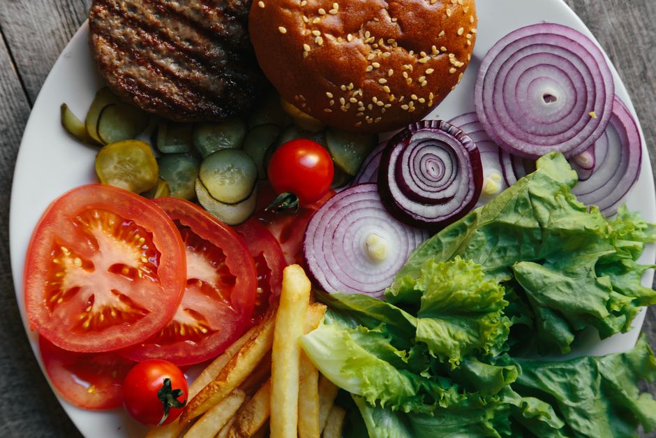 Top view of burger plate with fresh vegetables, fries, and ingredients.