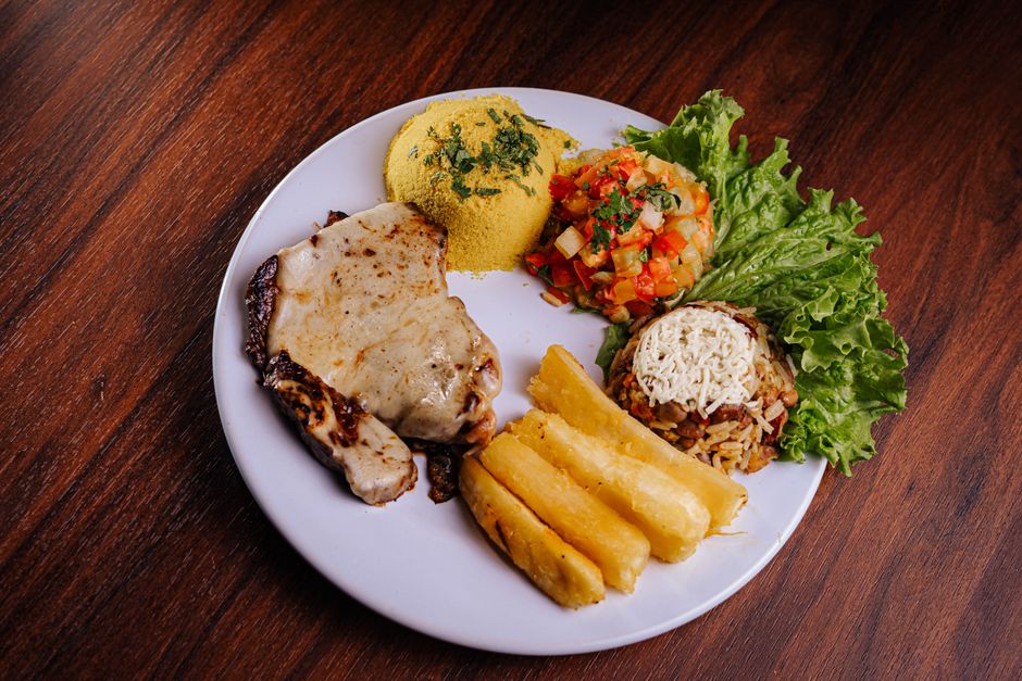 A delicious plate of Brazilian cuisine featuring pork chop, rice, beans, and fresh salad.