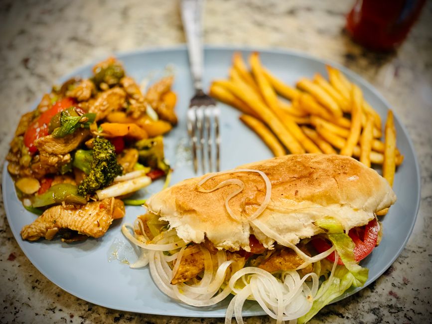Tasty chicken sandwich served with fries and colorful stir-fried vegetables on a blue plate.