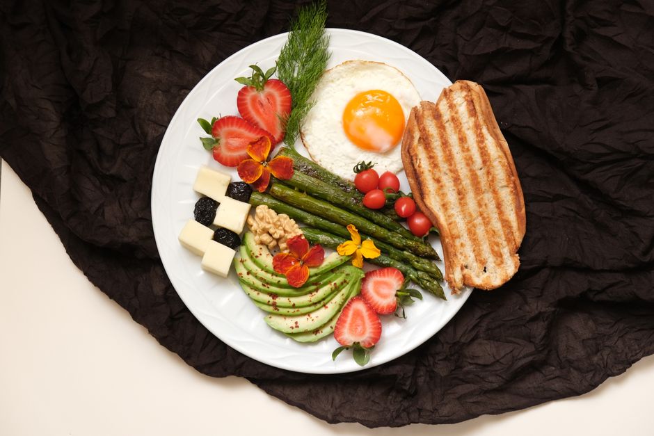 A nutritious breakfast featuring a fried egg, fresh vegetables, and toast on a white plate.