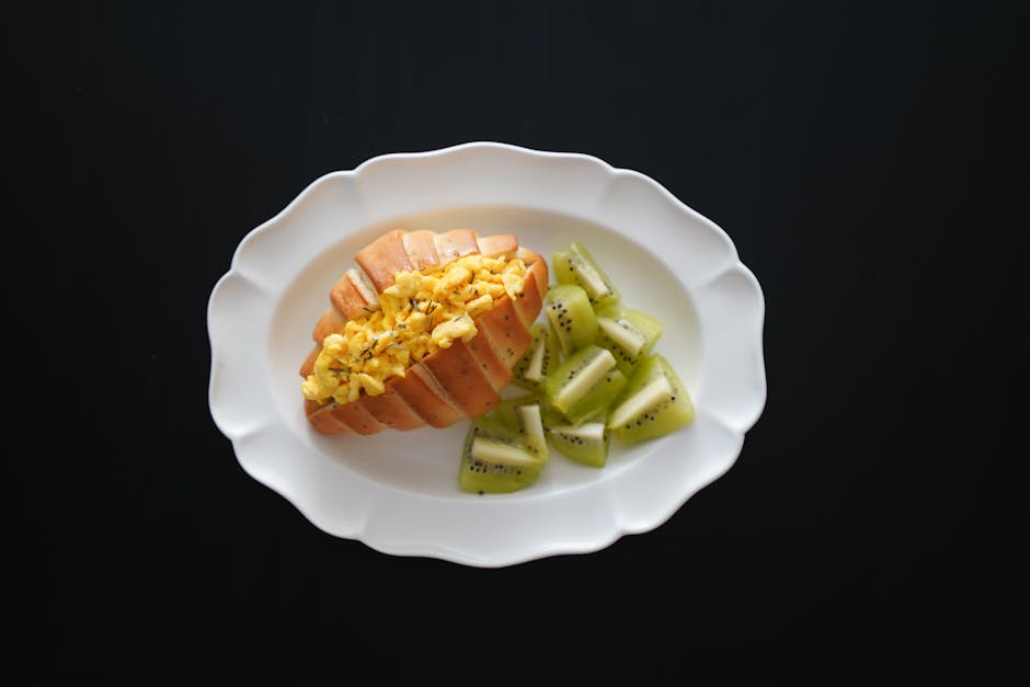 A delicious breakfast of scrambled eggs on toast paired with fresh kiwi slices on a white platter.