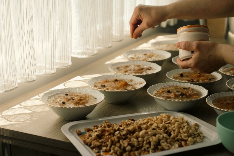 Person adding toppings to bowls of oatmeal on a sunlit table, featuring nuts and raisins.