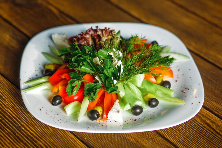 Colorful vegetable salad with fresh herbs and black olives on a white plate.