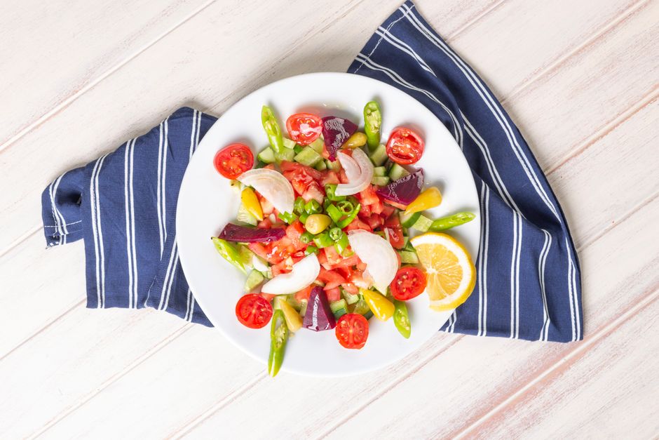 Colorful Turkish salad with fresh vegetables and lemon on a white plate, top view.